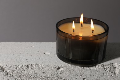 Photo of Burning soy wax candle on concrete block against gray background, closeup. Space for text