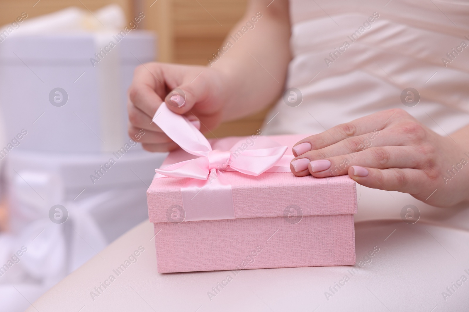 Photo of Bride opening beautiful wedding gift indoors, closeup