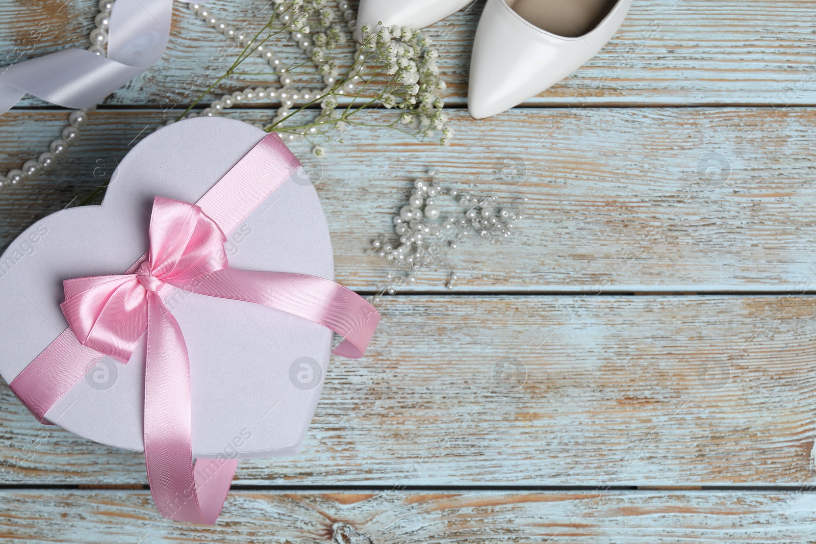 Photo of Beautiful wedding gift, pearl jewelry, ribbon, bridal shoes and gypsophila flowers on wooden table, flat lay. Space for text