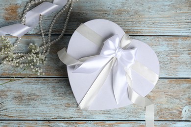 Photo of Beautiful wedding gift, pearl jewelry, ribbon and gypsophila flowers on wooden table, flat lay