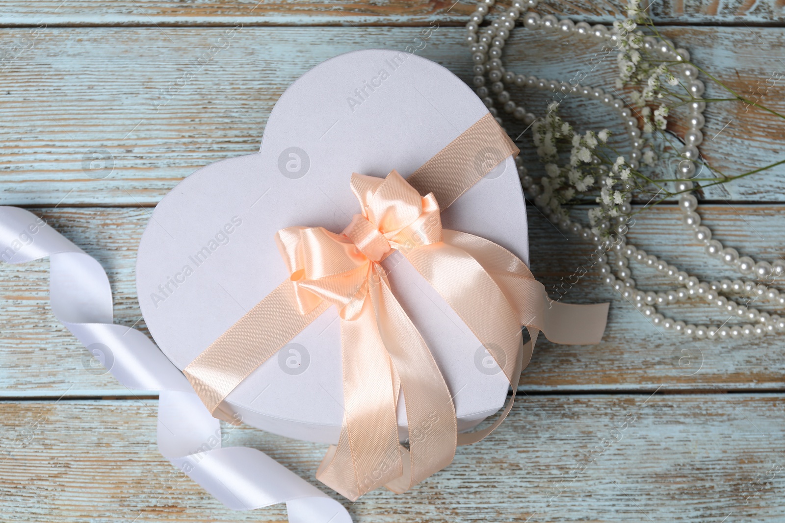 Photo of Beautiful wedding gift, pearl jewelry, ribbon and gypsophila flowers on wooden table, flat lay