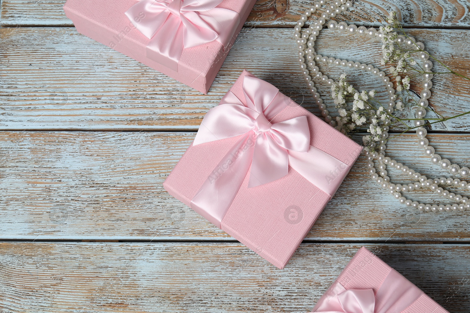 Photo of Beautiful wedding gifts, pearl jewelry and gypsophila flowers on wooden table, flat lay. Space for text