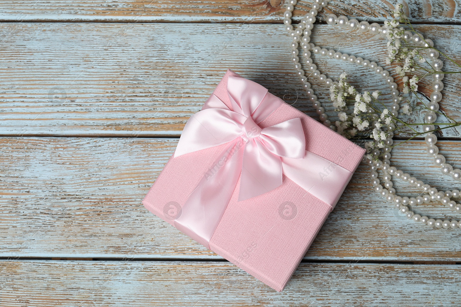 Photo of Beautiful wedding gift, pearl jewelry and gypsophila flowers on wooden table, flat lay. Space for text