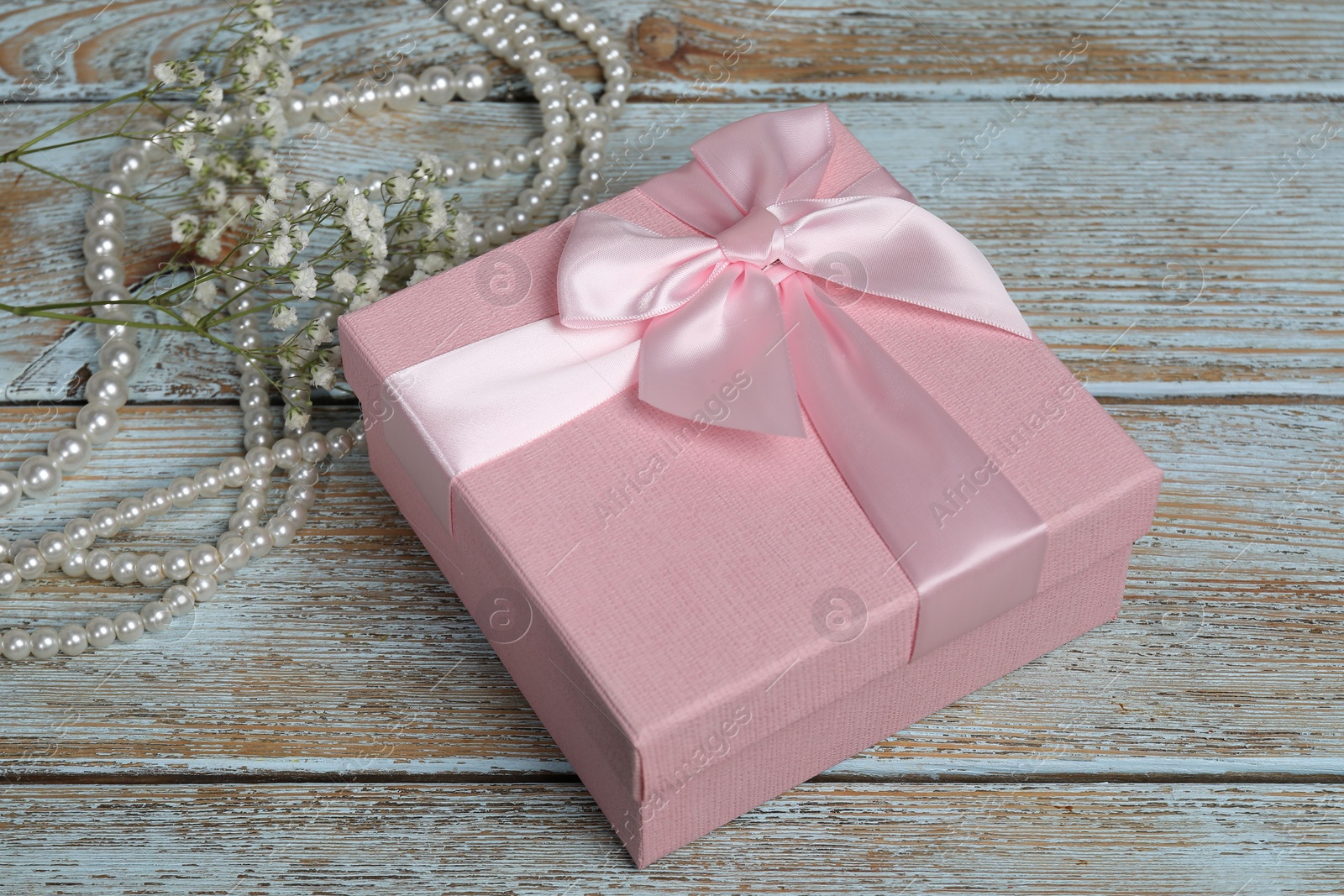 Photo of Beautiful wedding gift, pearl jewelry and gypsophila flowers on wooden table, closeup