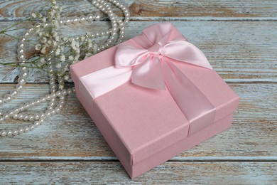 Photo of Beautiful wedding gift, pearl jewelry and gypsophila flowers on wooden table, closeup