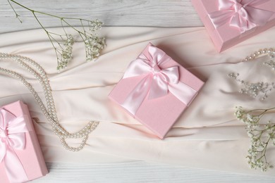 Photo of Beautiful wedding gifts, pearl jewelry, dress and gypsophila flowers on light wooden table, flat lay