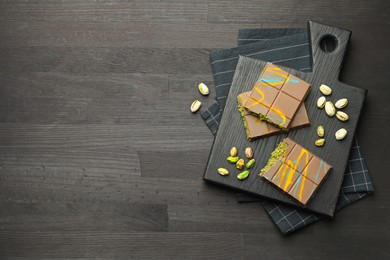 Photo of Pieces of Dubai chocolate bars with pistachios and knafeh on black wooden table, flat lay