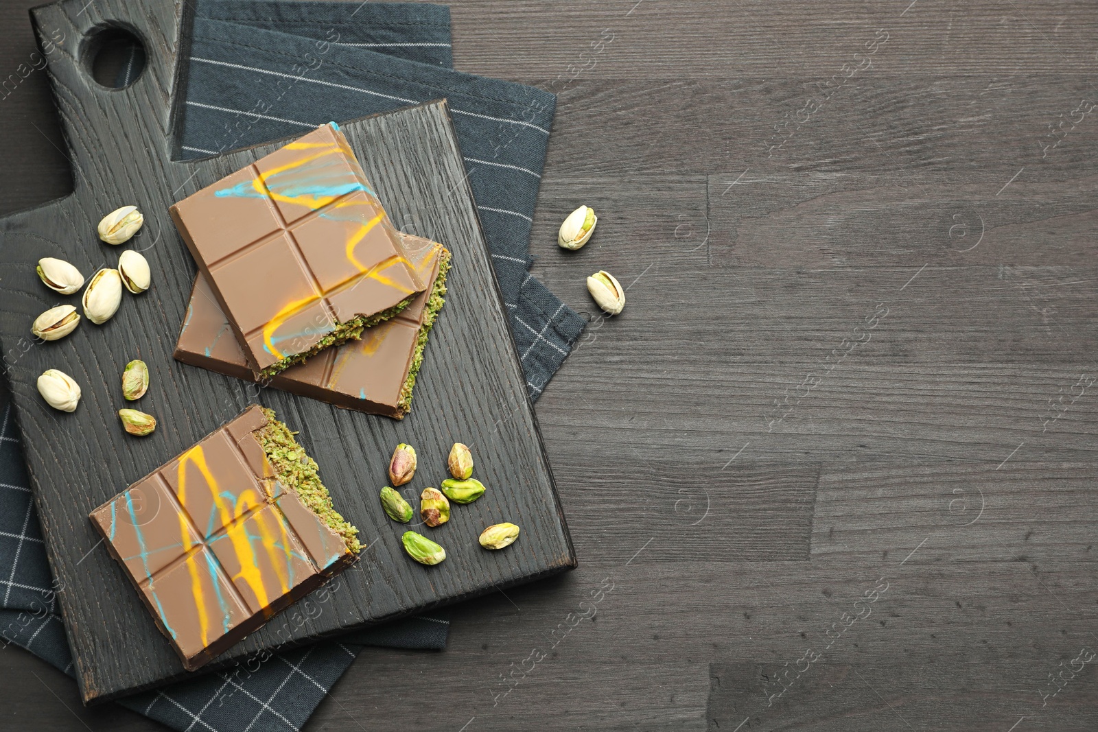 Photo of Pieces of Dubai chocolate bars with pistachios and knafeh on black wooden table, flat lay