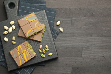 Photo of Pieces of Dubai chocolate bars with pistachios and knafeh on black wooden table, flat lay