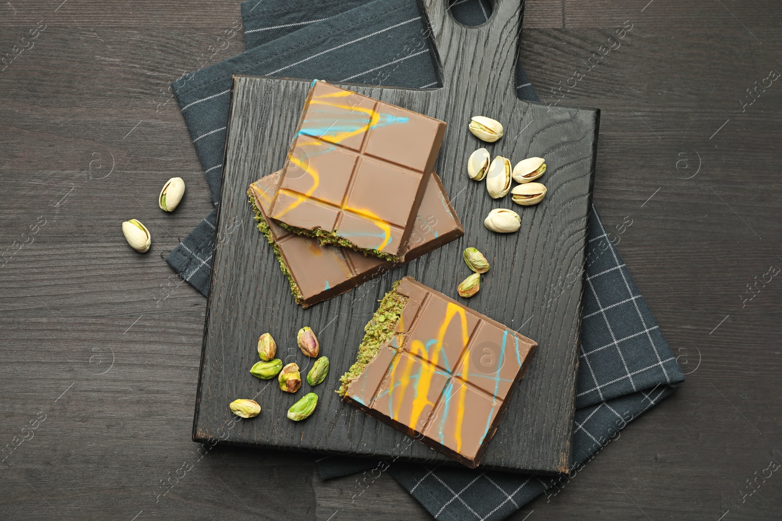 Photo of Pieces of Dubai chocolate bars with pistachios and knafeh on black wooden table, top view