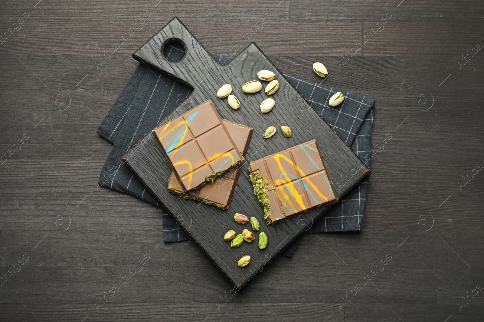 Photo of Pieces of Dubai chocolate bars with pistachios and knafeh on black wooden table, top view