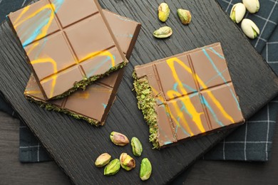 Photo of Pieces of Dubai chocolate bars with pistachios and knafeh on black wooden table, flat lay