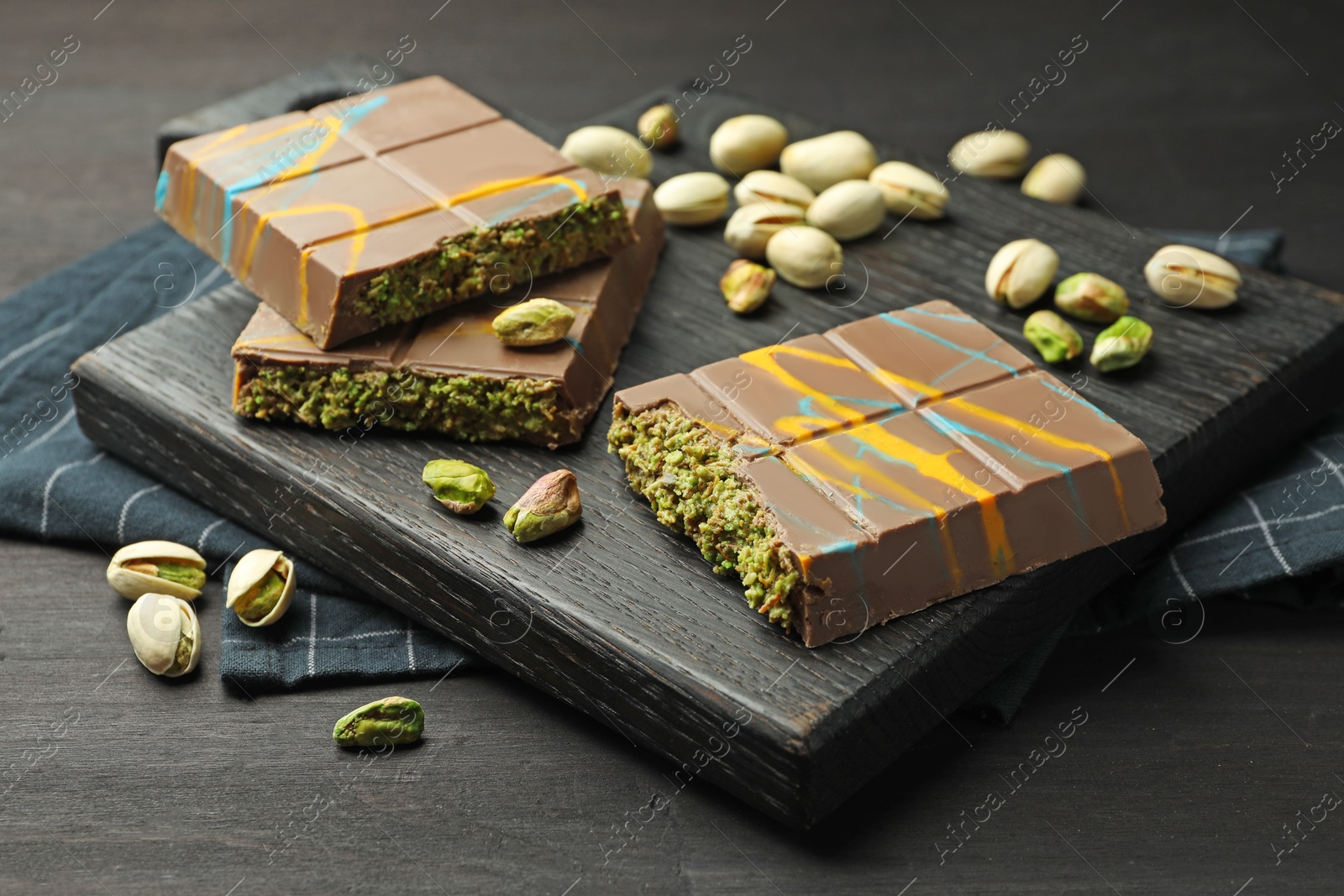 Photo of Pieces of Dubai chocolate bars with pistachios and knafeh on black wooden table, closeup