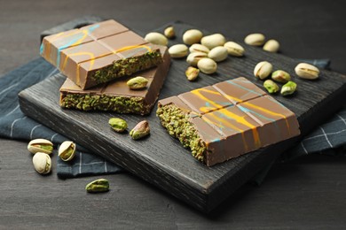 Photo of Pieces of Dubai chocolate bars with pistachios and knafeh on black wooden table, closeup