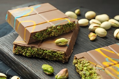 Photo of Pieces of Dubai chocolate bars with pistachios and knafeh on black table, closeup