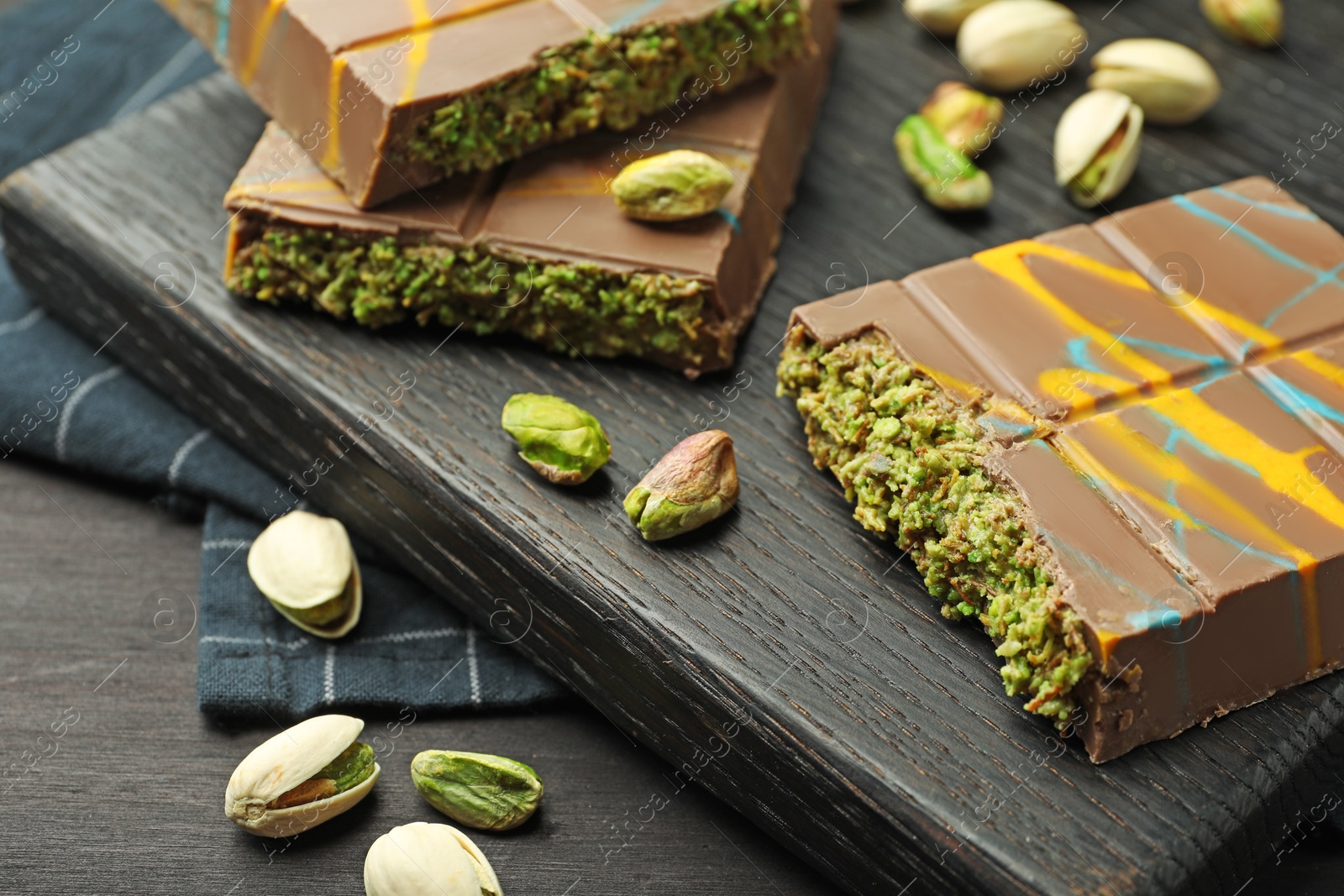 Photo of Pieces of Dubai chocolate bars with pistachios and knafeh on black wooden table, closeup