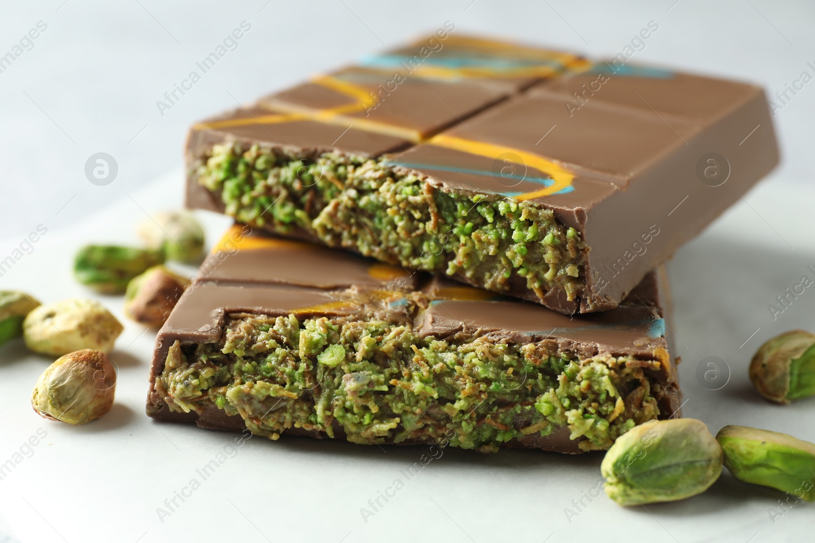 Photo of Pieces of Dubai chocolate bar with pistachios and knafeh on light grey table, closeup