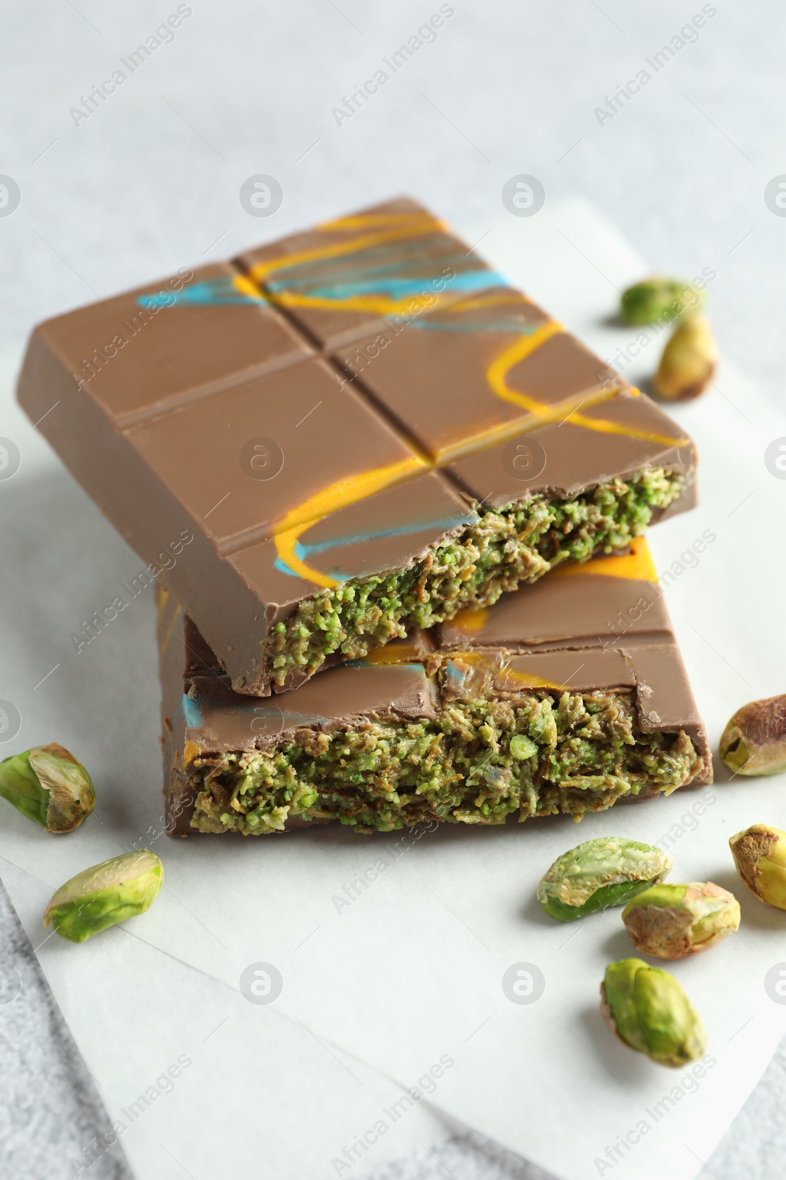 Photo of Pieces of Dubai chocolate bar with pistachios and knafeh on light grey table, closeup