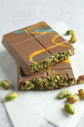 Photo of Pieces of Dubai chocolate bar with pistachios and knafeh on light grey table, closeup