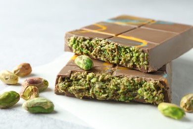 Photo of Pieces of Dubai chocolate bar with pistachios and knafeh on light grey table, closeup