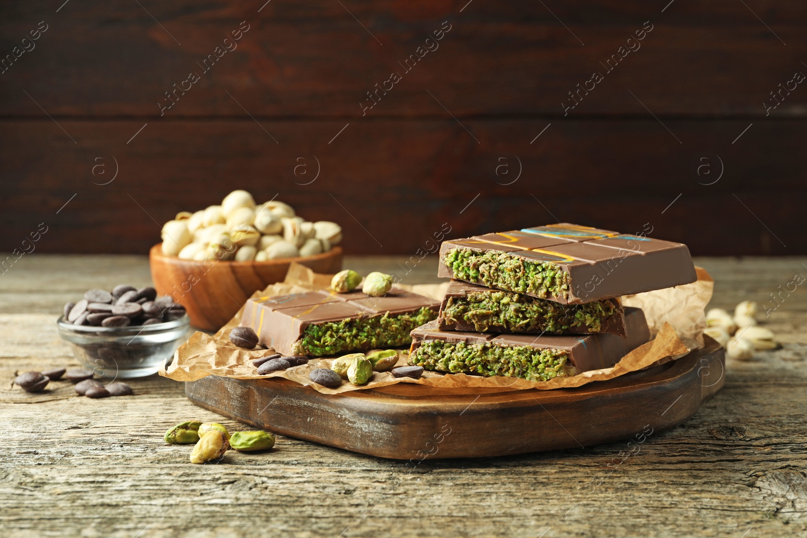 Photo of Pieces of Dubai chocolate bar with pistachios, knafeh and cacao chips on wooden table, closeup