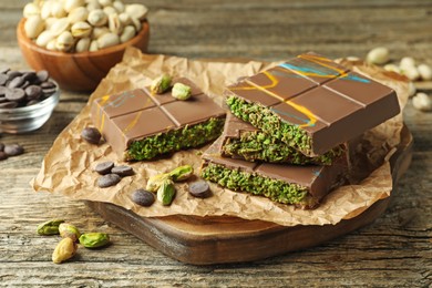 Photo of Pieces of Dubai chocolate bar with pistachios, knafeh and cacao chips on wooden table, closeup