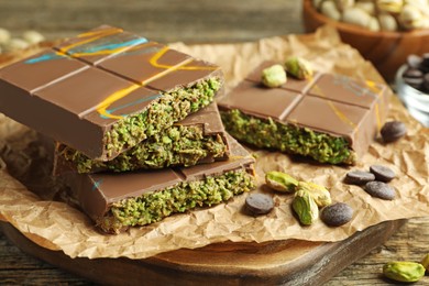 Photo of Pieces of Dubai chocolate bar with pistachios, knafeh and cacao chips on wooden table, closeup