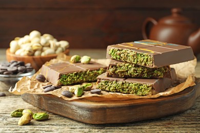 Photo of Pieces of Dubai chocolate bar with pistachios, knafeh and cacao chips on wooden table, closeup