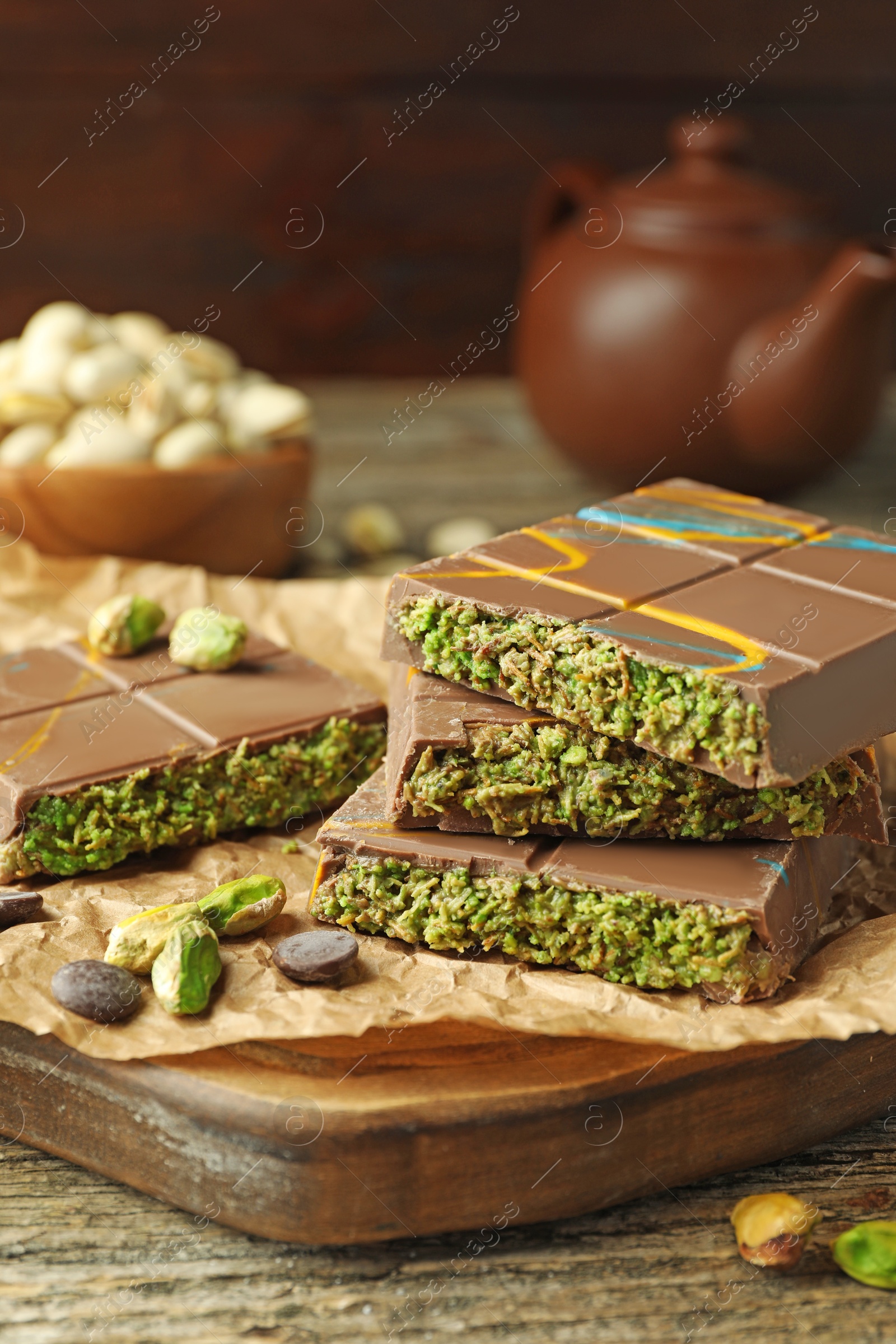 Photo of Pieces of Dubai chocolate bar with pistachios, knafeh and cacao chips on wooden table, closeup