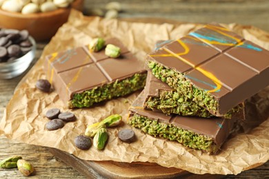 Photo of Pieces of Dubai chocolate bar with pistachios, knafeh and cacao chips on wooden table, closeup