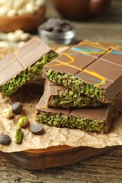 Photo of Pieces of Dubai chocolate bar with pistachios, knafeh and cacao chips on wooden table, closeup