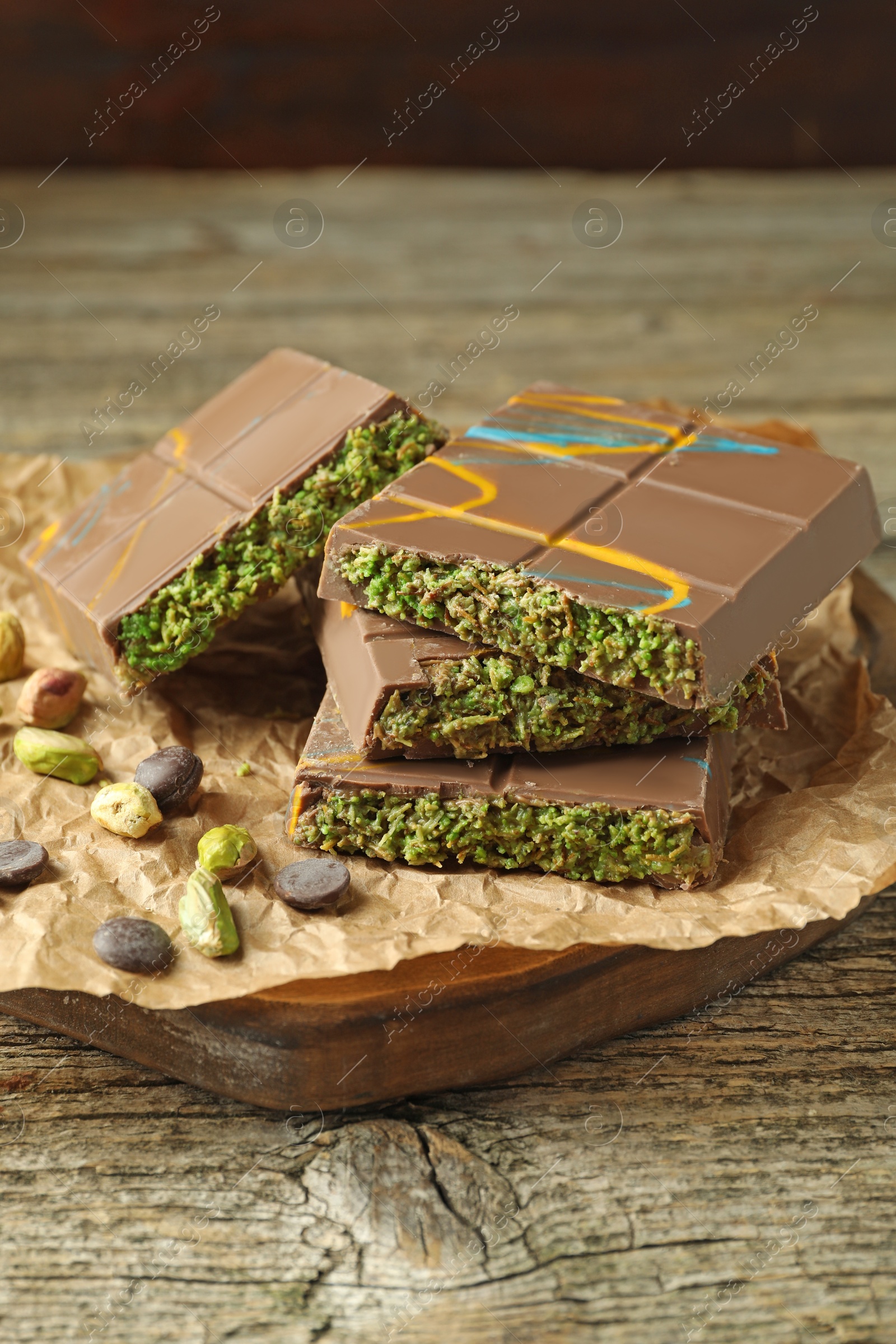 Photo of Pieces of Dubai chocolate bar with pistachios, knafeh and cacao chips on wooden table, closeup