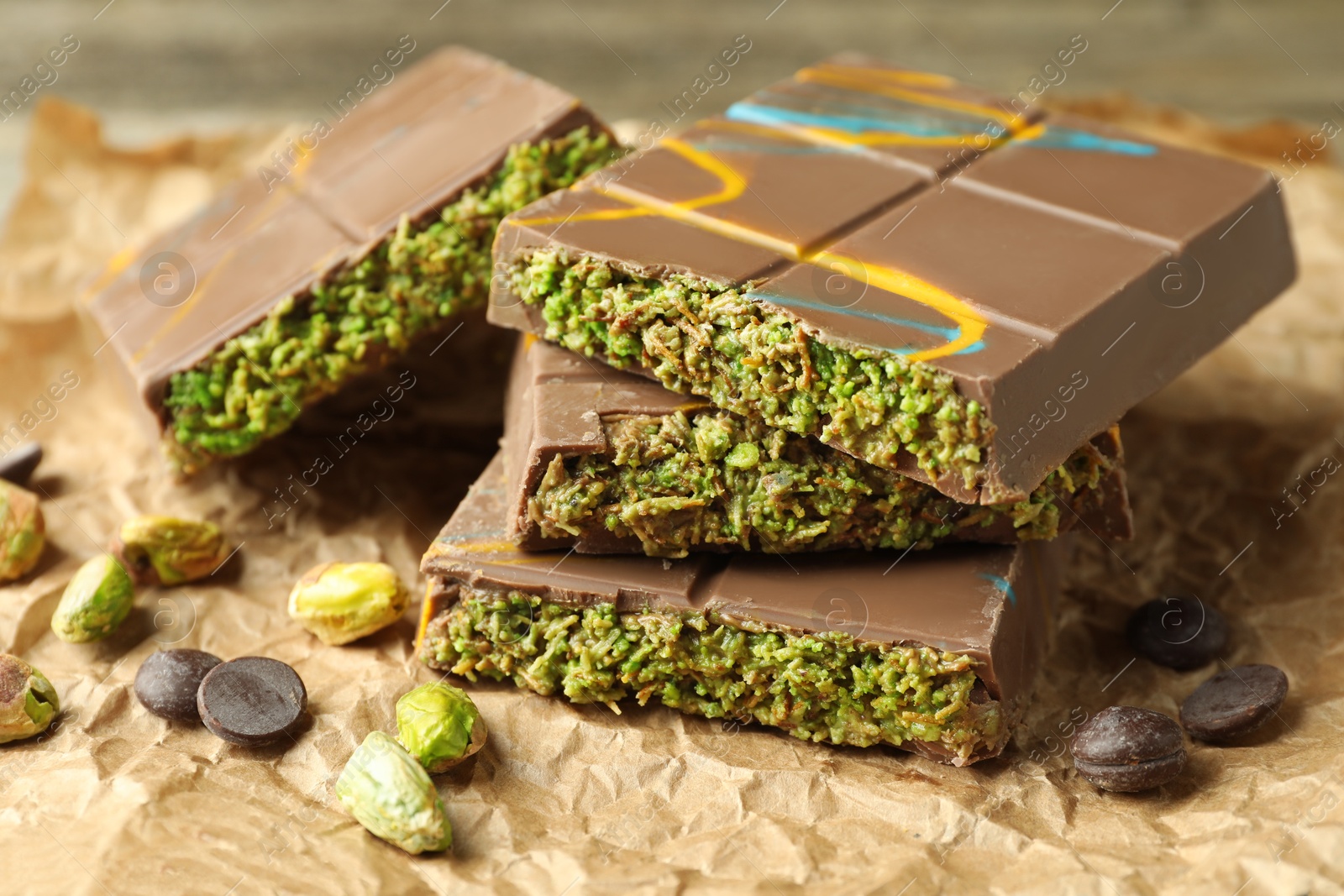 Photo of Pieces of Dubai chocolate bar with pistachios, knafeh and cacao chips on table, closeup