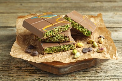 Photo of Pieces of Dubai chocolate bar with pistachios, knafeh and cacao chips on wooden table, closeup