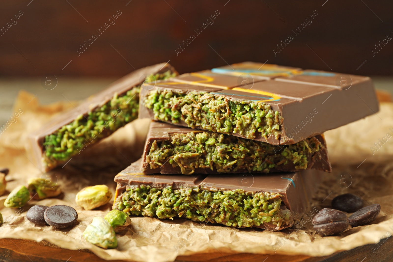 Photo of Pieces of Dubai chocolate bar with pistachios, knafeh and cacao chips on table, closeup