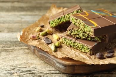 Photo of Pieces of Dubai chocolate bar with pistachios, knafeh and cacao chips on wooden table, closeup