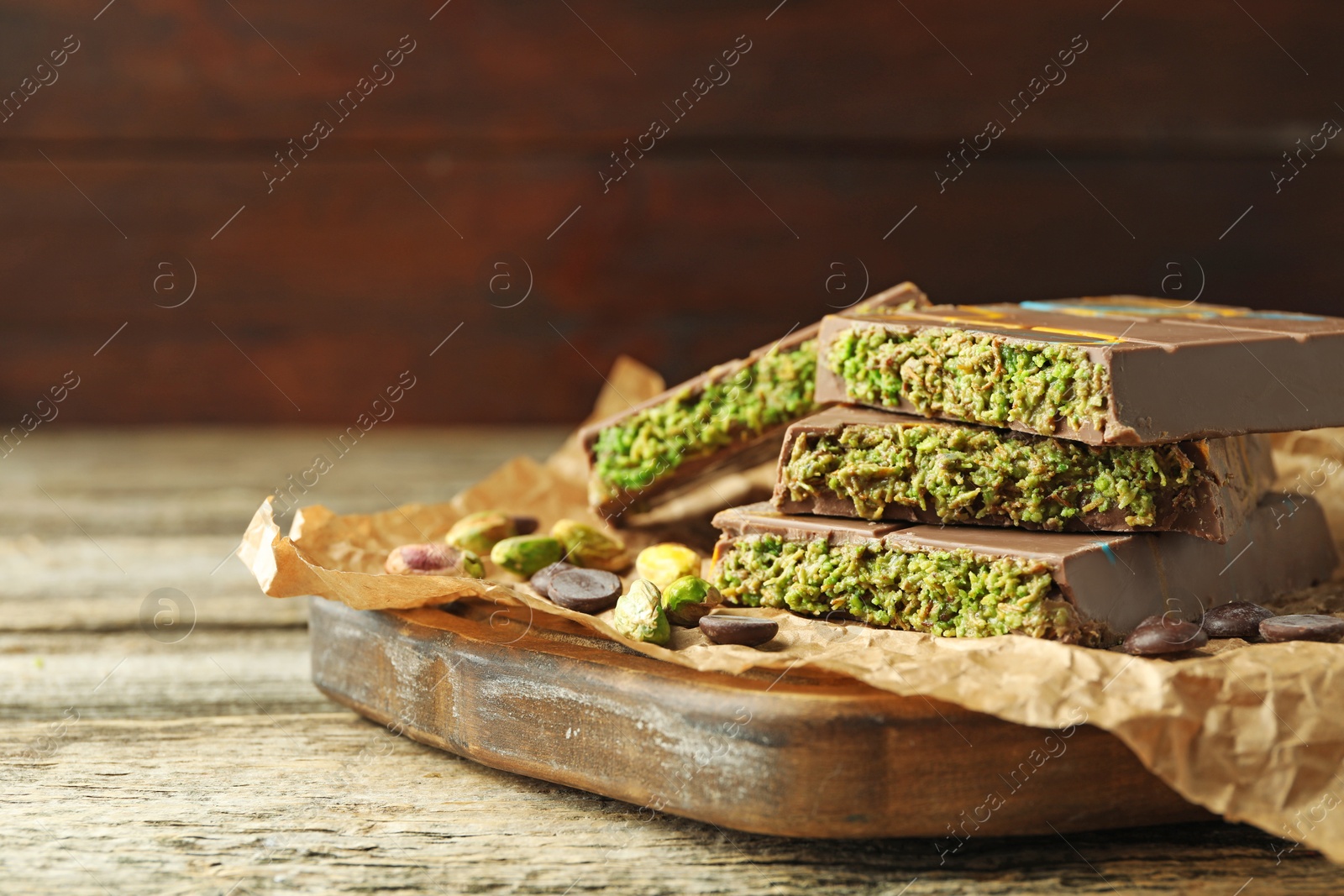 Photo of Pieces of Dubai chocolate bar with pistachios, knafeh and cacao chips on wooden table, closeup. Space for text