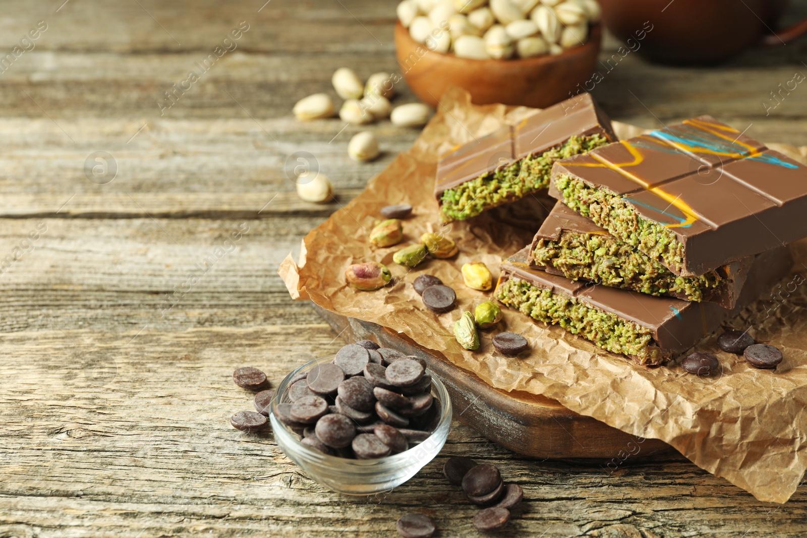 Photo of Pieces of Dubai chocolate bar with pistachios, knafeh and cacao chips on wooden table, closeup. Space for text