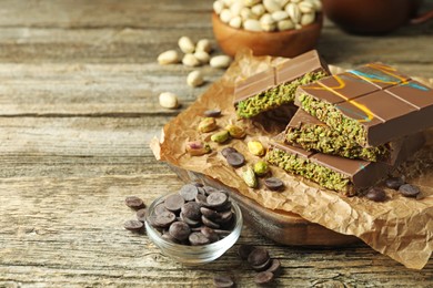 Photo of Pieces of Dubai chocolate bar with pistachios, knafeh and cacao chips on wooden table, closeup. Space for text