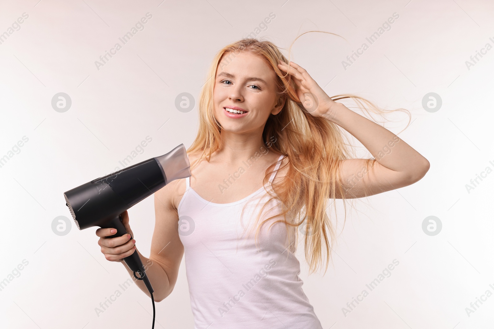 Photo of Beautiful young woman drying her hair with hairdryer on light grey background