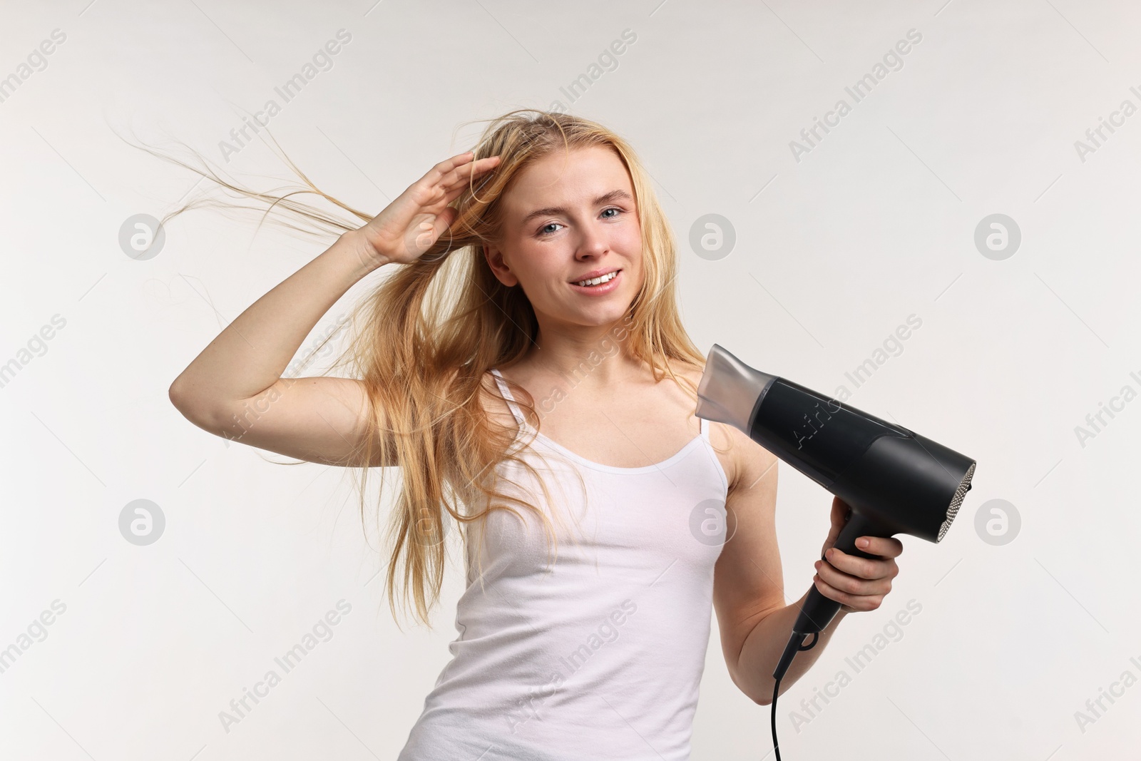 Photo of Beautiful young woman drying her hair with hairdryer on light grey background