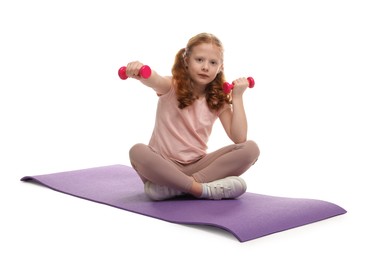 Photo of Cute little girl with dumbbells on fitness mat against white background