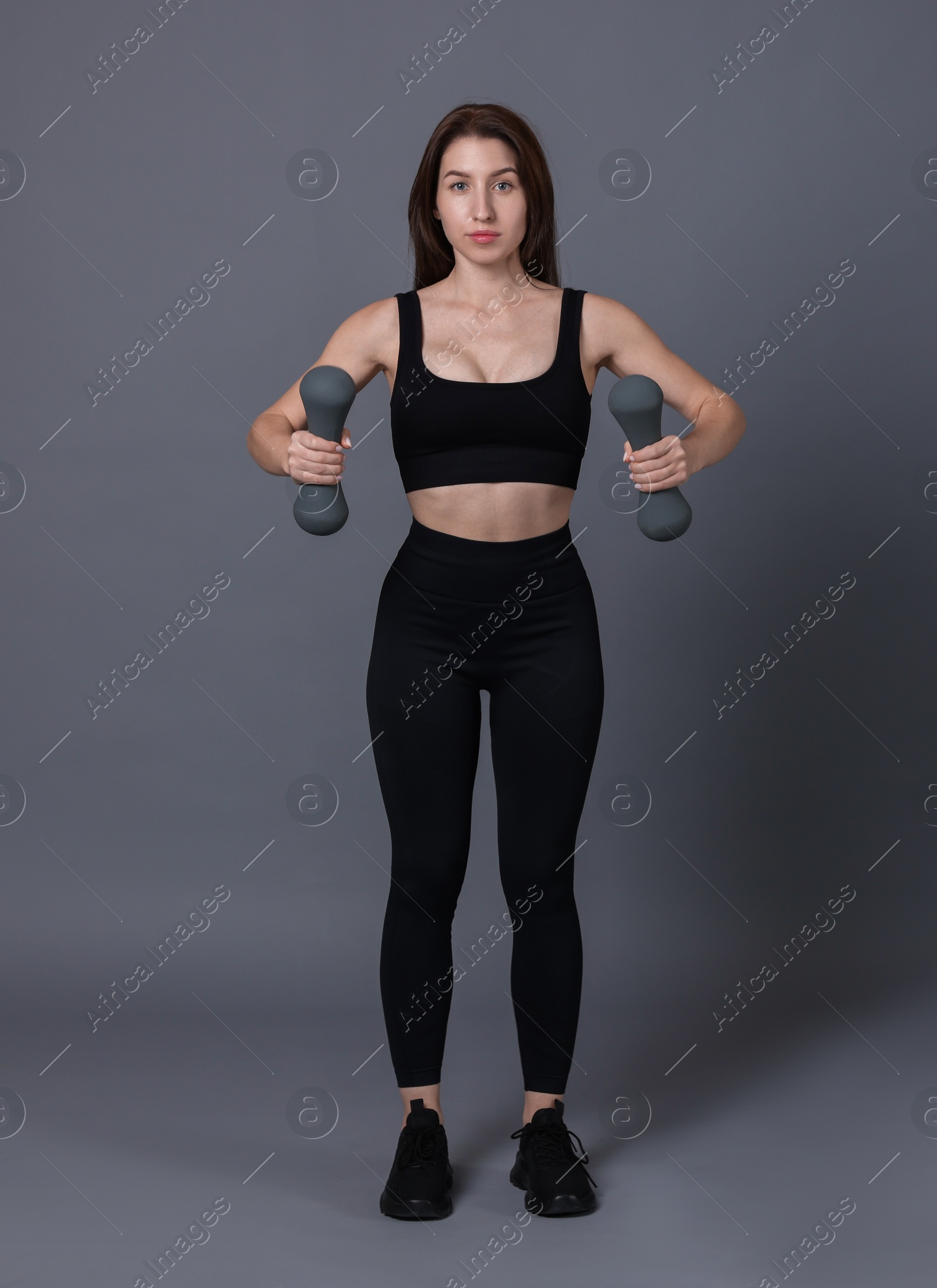 Photo of Woman in sportswear exercising with dumbbells on grey background