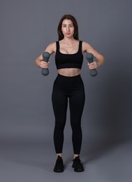 Photo of Woman in sportswear exercising with dumbbells on grey background