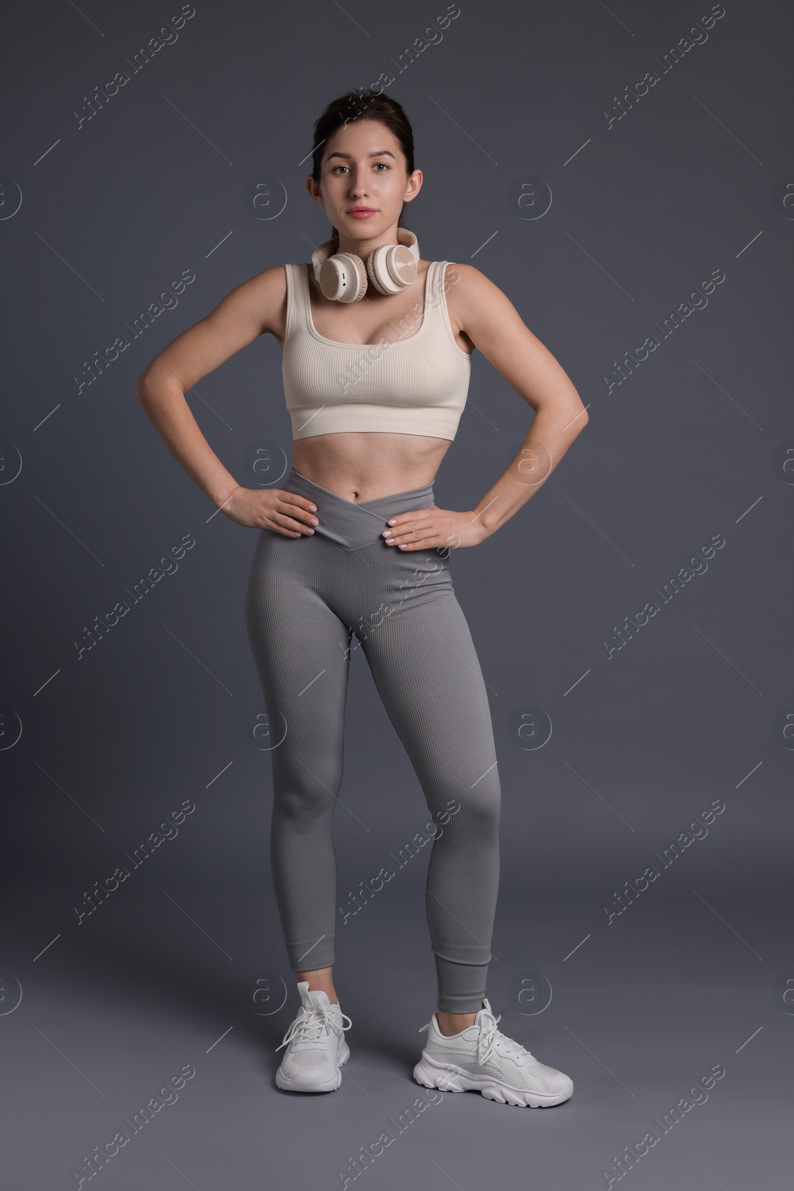 Photo of Woman in sportswear with headphones on grey background