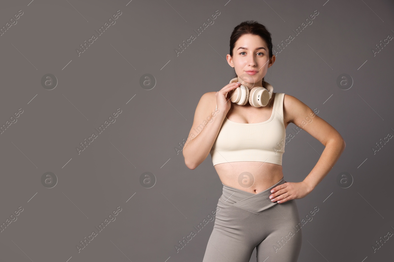 Photo of Woman in sportswear with headphones on grey background, space for text