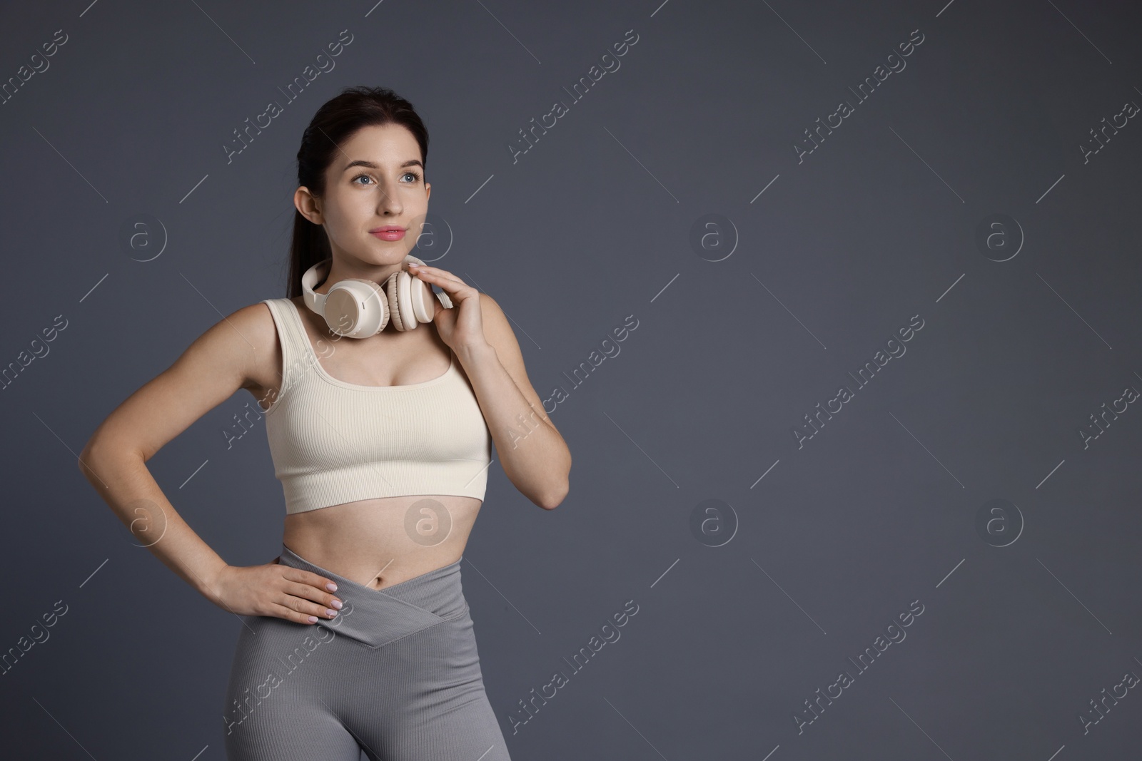 Photo of Woman in sportswear with headphones on grey background, space for text