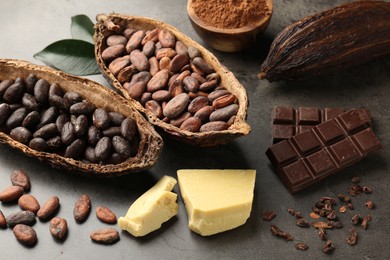 Cocoa pods with beans, chocolate, butter and leaves on grey background, closeup