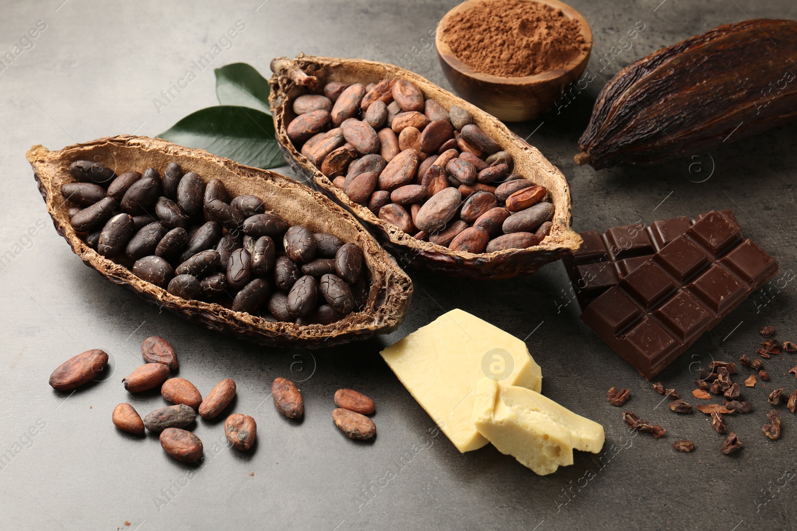 Photo of Cocoa pods with beans, chocolate, butter and leaves on grey background