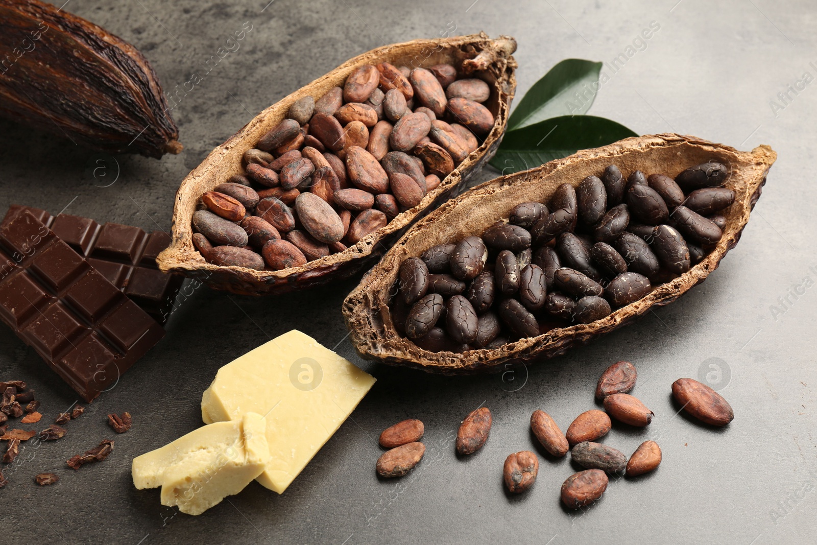 Photo of Cocoa pods with beans, chocolate, butter and leaves on grey background